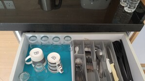 Un tiroir de cuisine contenant un tapis bleu, des tasses blanches, des verres transparents et divers ustensiles.