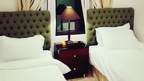 Une chambre d’hôtel avec deux lits, une table de chevet, une lampe, un appareil de climatisation et une fenêtre avec des rideaux.