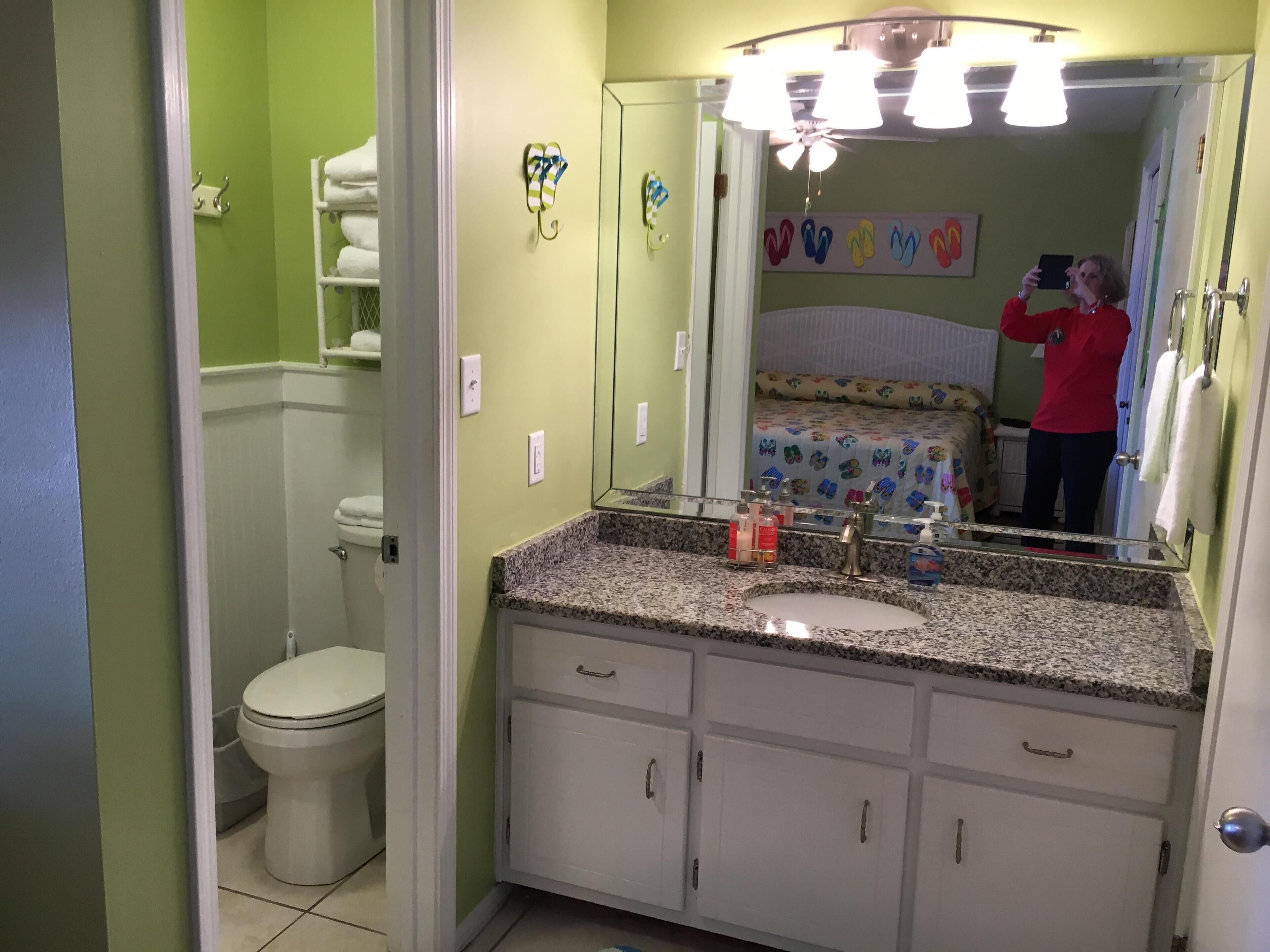 Un baño con inodoro blanco, lavamanos con encimera de granito y un espejo encima.