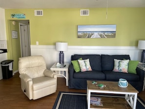 A living room with a beige sofa, a dark grey couch, a small wooden coffee table, and a painting of a beach scene.