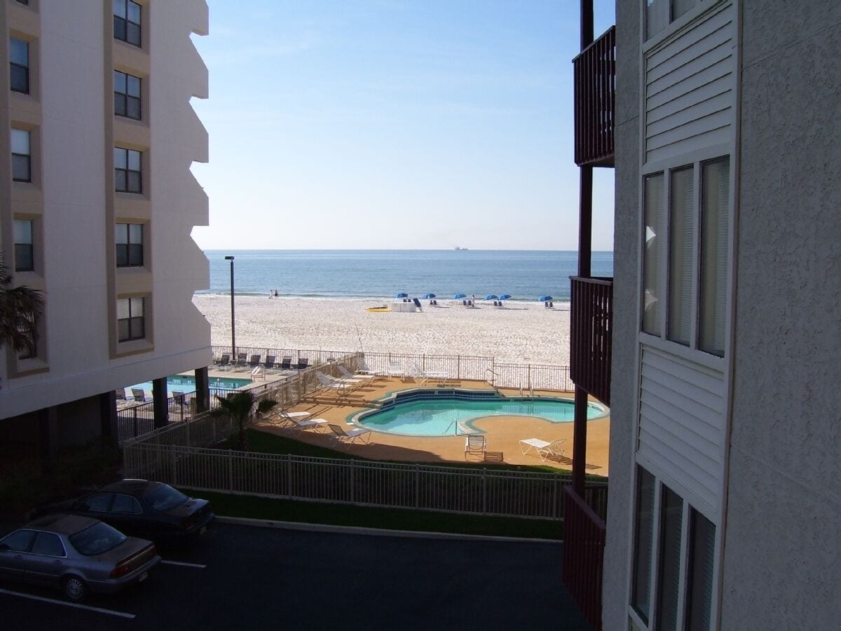 Vue depuis un balcon donnant sur une plage, avec une piscine et des chaises longues.