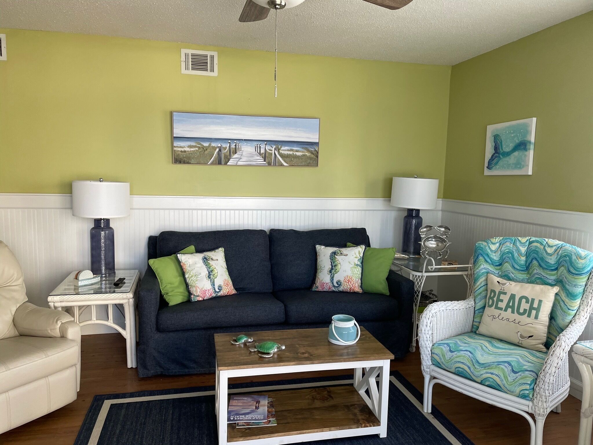 A living room with a sofa, armchairs, a coffee table, and a painting of a beach scene.