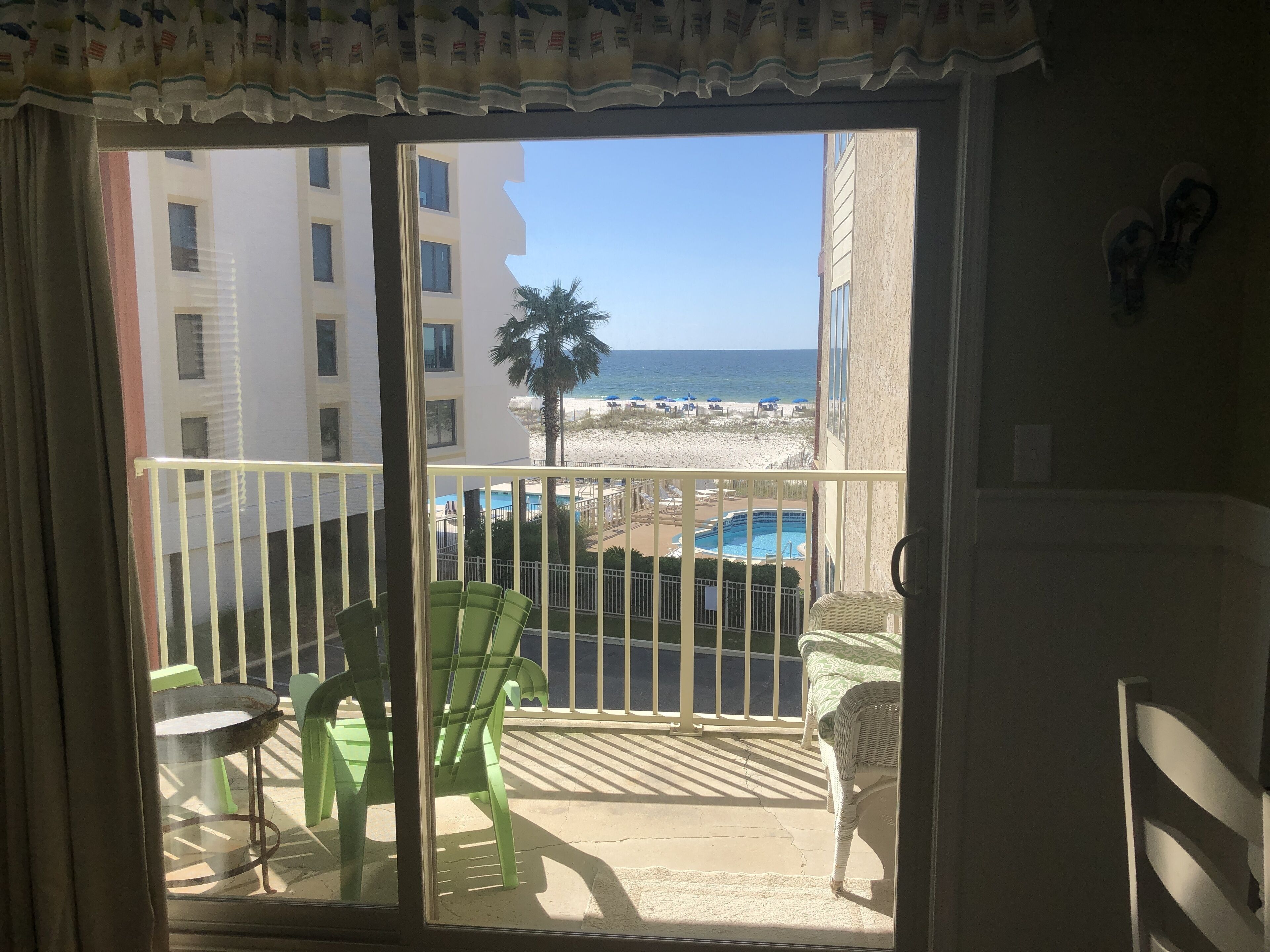 Een balkon met uitzicht op een strand, zwembad en gebouwen.