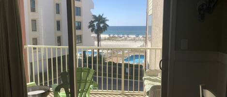 Een balkon met uitzicht op een strand, zwembad en gebouwen.