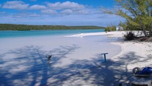 Ein Strand mit klarem türkisblauem Wasser, weißem Sand und ein paar Bäumen, die Schatten werfen.