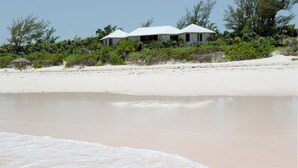 Ein Strandgrundstück mit einem weißen Haus, Sandstrand und dichter Bepflanzung.