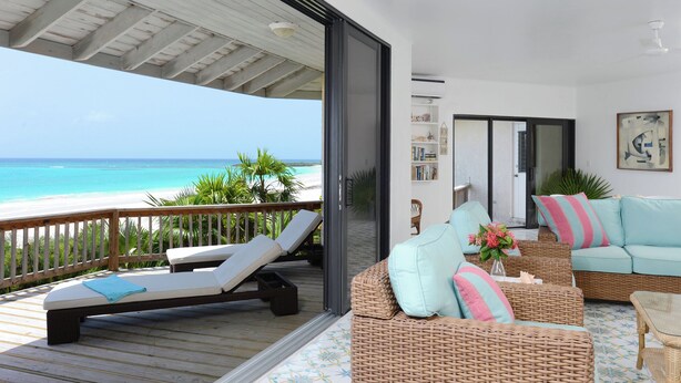 Ein Balkon mit Blick auf den Strand, eine Rattan-Couch mit Kissen und ein Bücherregal.