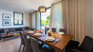Un comedor moderno con una mesa de madera dispuesta para seis personas, rodeada de sillas. Se observa un sofá y una pequeña mesa de centro al fondo.