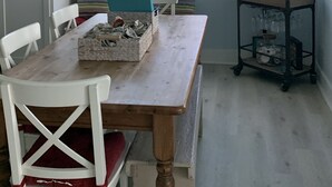 Un coin repas avec une table en bois, des chaises blanches, un coussin à rayures et une fenêtre donnant sur le toit.