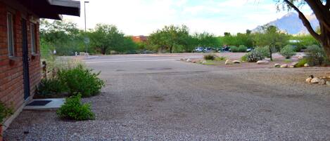 A parking lot with a building on the left, surrounded by gravel and small plants.