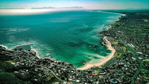 Vista aérea de uma cidade costeira com praia, estradas e áreas residenciais.