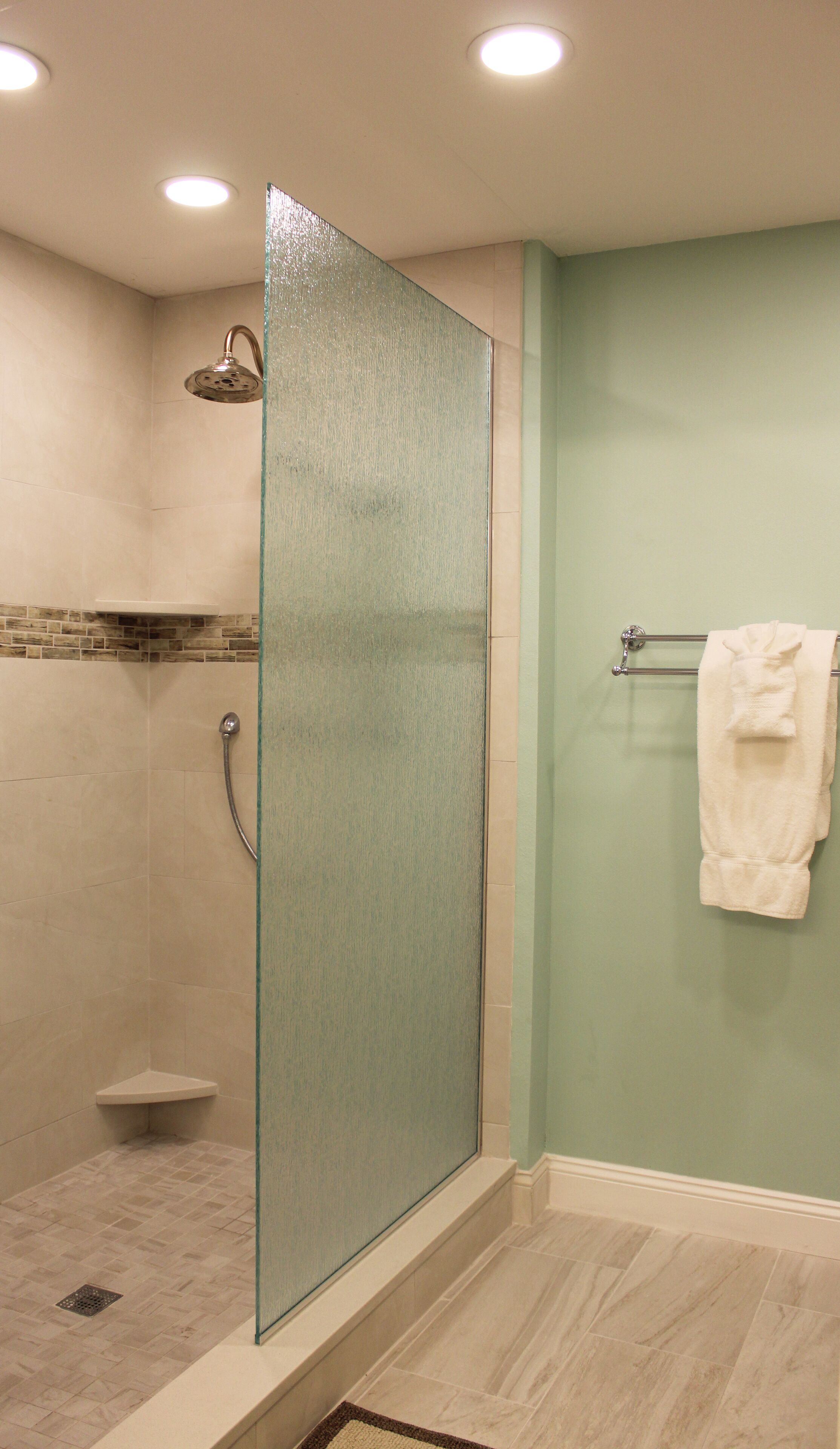 A bathroom with a glass shower enclosure, a towel rack with a white towel, and a tiled floor.