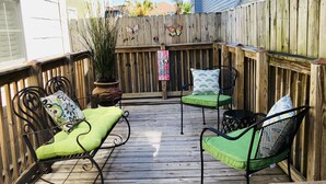 Una terraza de madera con dos sillas verdes acolchadas y una pequeña mesa, rodeada por una valla de madera.