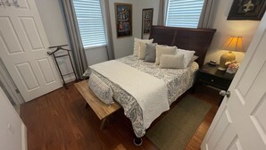 Un dormitorio ordenado con cama, mesita de noche, lámpara y una puerta.