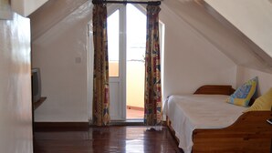 Une chambre à coucher avec un lit en bois, une télévision et une vue sur l’extérieur, visible à travers une fenêtre ornée de rideaux à motifs.