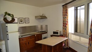 Une cuisine compacte avec des meubles en bois, une cuisinière encastrée, un four à micro-ondes et une fenêtre agrémentée de rideaux à motifs.
