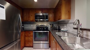 A kitchen with stainless steel appliances, wooden cabinets, a granite countertop, and a double sink.
