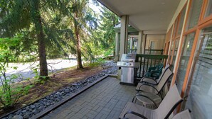 An outdoor patio with a grill, chairs, and a view of a lake surrounded by trees. - Stoney Creek Northstar - Renovated, Ground Floor Condo in Whistler Village. (Whistler)