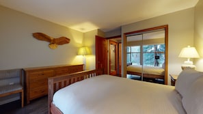 A bedroom with a bed, a wooden bench, a dresser, a mirror, and a window with a view of trees.