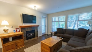 A living room with a fireplace, a television mounted above it, a sofa, and a coffee table. - Stoney Creek Northstar - Renovated, Ground Floor Condo in Whistler Village. (Whistler)