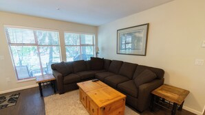 A living room with a sectional sofa, a wooden coffee table, a small side table, and a framed picture on the wall. - Stoney Creek Northstar - Renovated, Ground Floor Condo in Whistler Village. (Whistler)