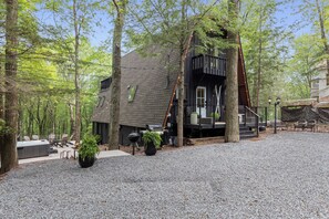 Eine Hütte mit einer Terrasse, Sitzgelegenheiten im Freien und einem Grillplatz, umgeben von Bäumen.