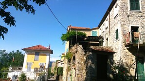 Une rue étroite bordée d’immeubles en pierre, dont l’un possède un balcon et une façade jaune, et l’autre, un toit recouvert de tuiles rouges.
