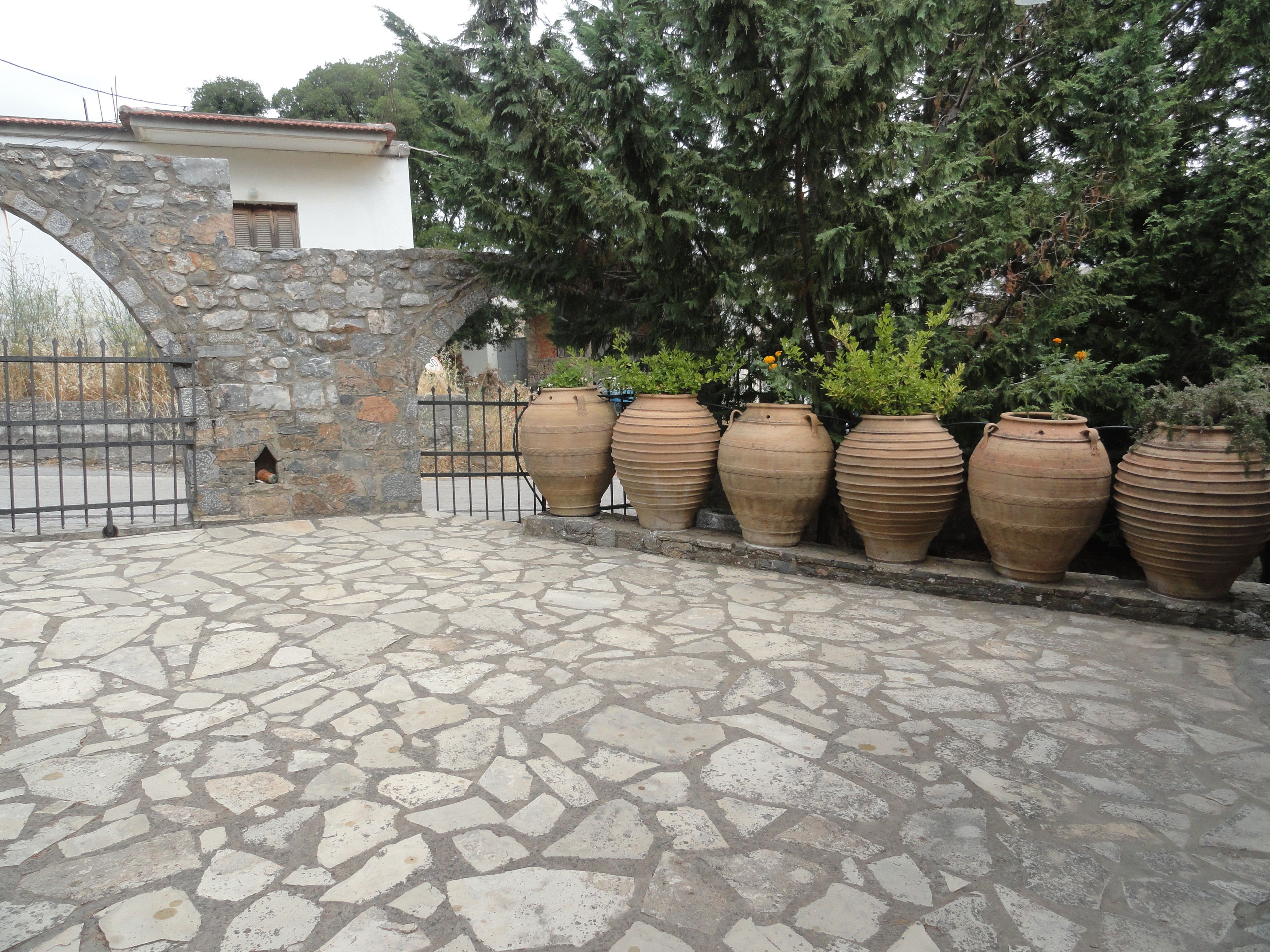 Um pátio com piso de pedra, uma parede de pedra e grandes vasos de terracota alinhados.
