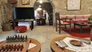 A rustic living room with a stone wall, a television, a chessboard, and a sofa with patterned cushions. - Zeus House Gaia (Lasithi Plateau)