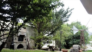 A rustic courtyard with stone walls, a windmill, and potted plants. - Zeus House Gaia (Lasithi Plateau)