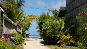 Un sentier étroit menant à une plage, bordé d’une végétation luxuriante et d’un bâtiment en bois.