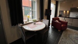 A modern kitchen with a built-in oven and microwave, a dining area with a round table and chairs, and a large window with curtains. - VRIJ van 29 augustus tot 5 september .2 pers studio 5 min lopen  het strand (Westkapelle)