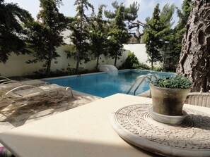 A swimming pool with lounge chairs and a decorative planter. - Villa Arokaria (Faistos)