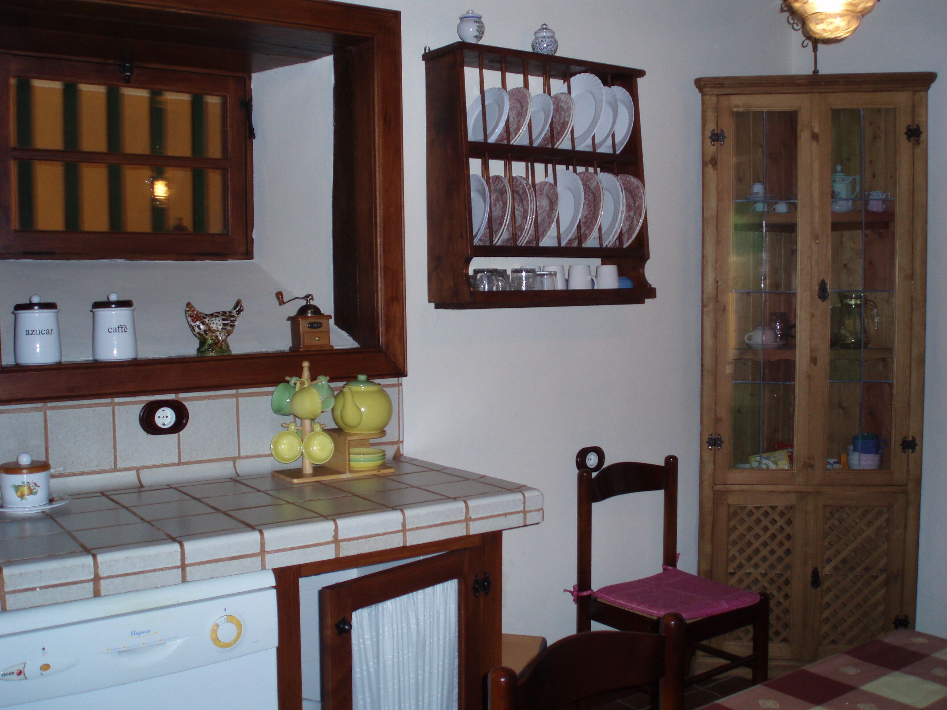 Una cocina con encimera de azulejos, una silla de madera, un armario con puertas de cristal y un espejo sobre la encimera.