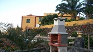 A stone barbecue grill with a chimney, surrounded by a stone wall and a palm tree. - Casa rural Villa Caya for 4 people (Orotava (La))