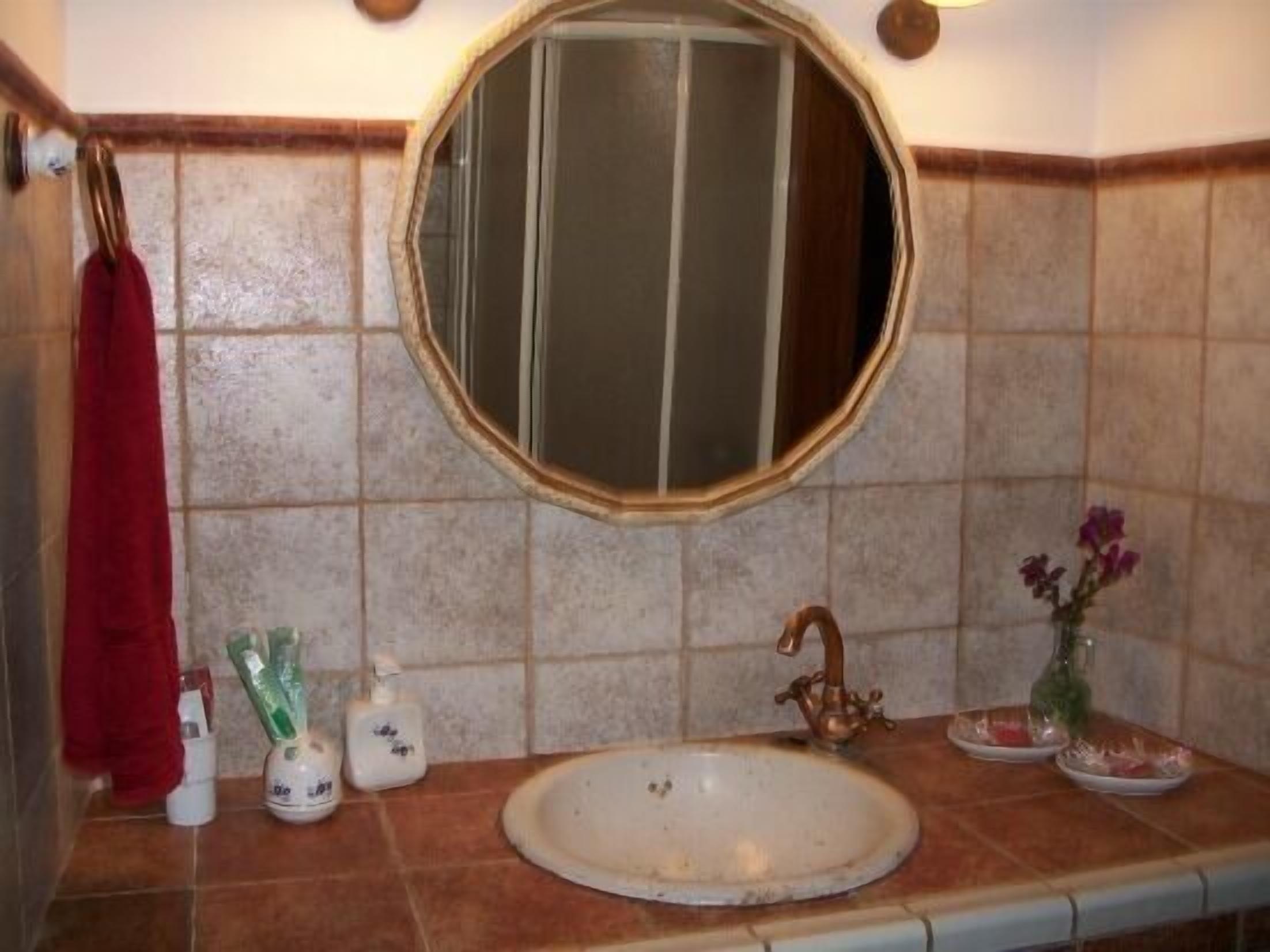 Une salle de bain avec un miroir rond, un lavabo et une serviette rouge suspendue à un porte-serviettes.