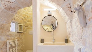 A bathroom with a stone wall, a round mirror, a sink, and a towel hanging on a hook.