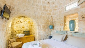A stone-walled bedroom with a bed, a wooden chair, a dresser, and a hanging light fixture.