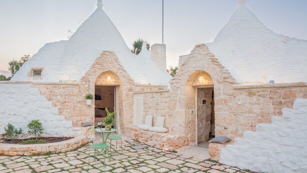 A traditional stone house with conical roofs, a paved courtyard, and a small outdoor seating area.