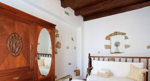 A bedroom with a wooden wardrobe, a bed with white linens, a stone wall, and a windmill decoration. - Villa Kamilari (Faistos)
