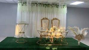 A stage with a green carpet, two chairs, a table, and a decorative backdrop. - Mi Tierra (Cabo Rojo)