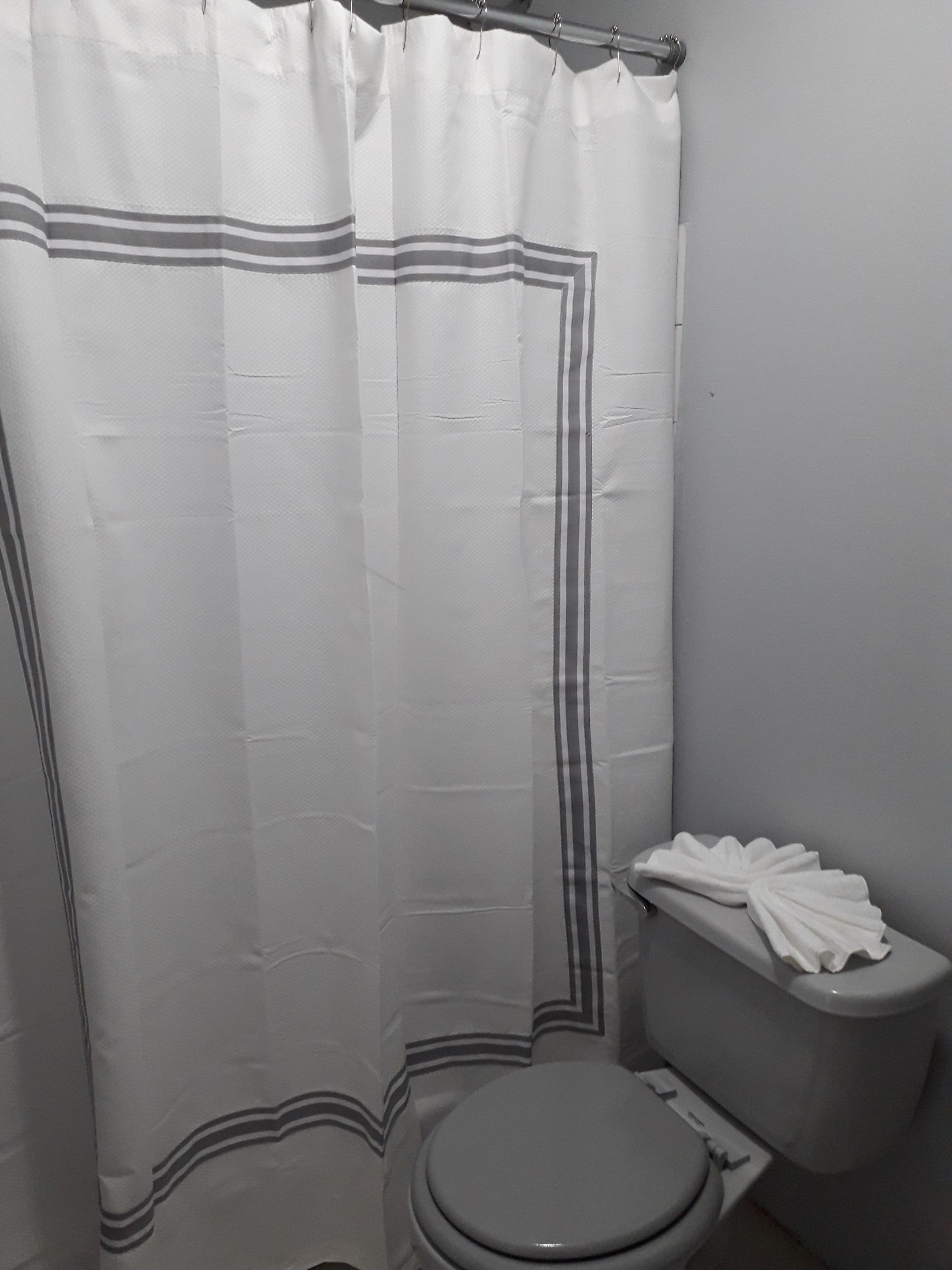 Un baño con cortina de ducha, inodoro y toallero con toallas.