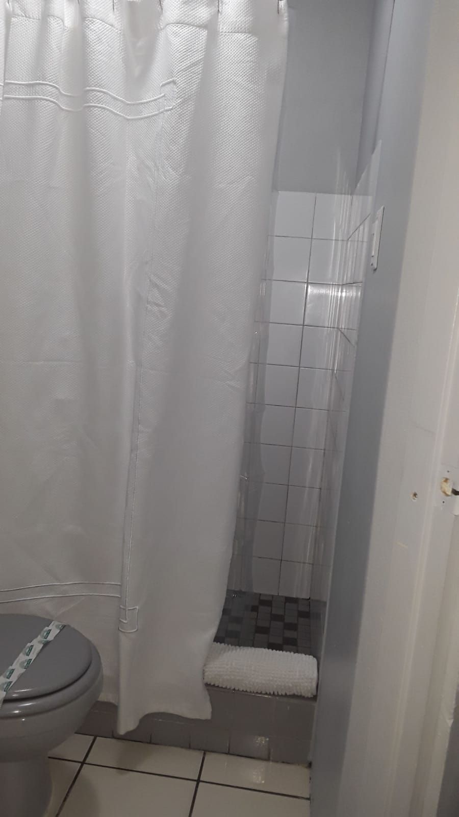 A bathroom with a toilet, a shower with tiled walls, and a white shower curtain.