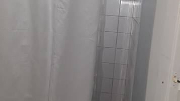 A bathroom with a toilet, a shower with tiled walls, and a white shower curtain.