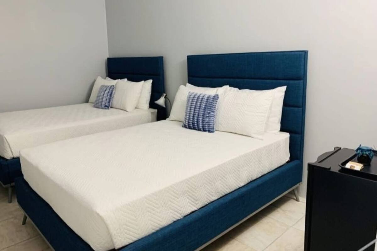 A hotel room with two beds, each with a blue headboard and white bedding.