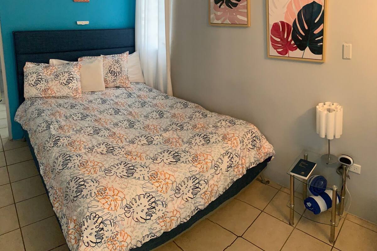 A bedroom with a bed, air conditioning unit, curtains, and two framed artworks.