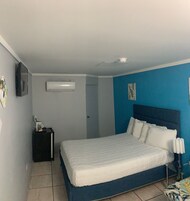 Quarto com cama, ar condicionado, mesa de cabeceira, abajur e porta.