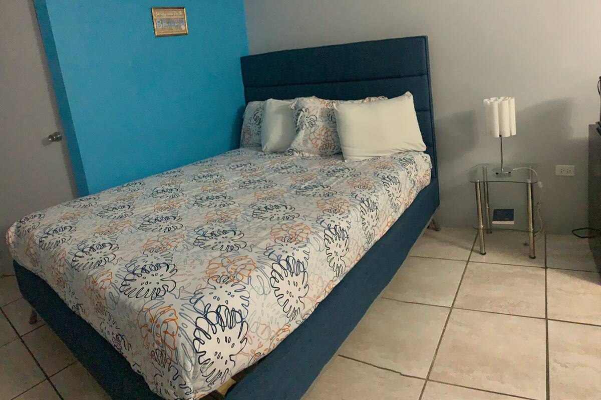 A bedroom with a bed, a nightstand, a lamp, and a wall-mounted air conditioner.