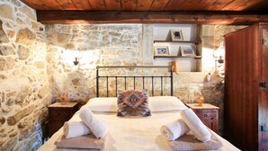 Ein Zimmer mit Steinsandsteinwand, Holzboden, einem Bett mit Handtüchern, einem Nachttisch, einem Regal mit Bildern und einem Holzschrank.