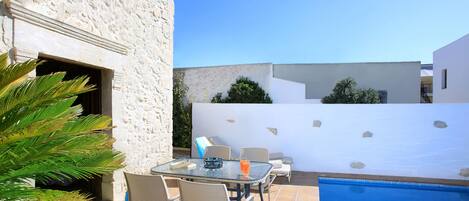 Un patio con una mesa y sillas de vidrio, una piscina y un muro de piedra.